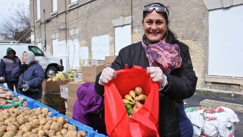 Philabundance volunteer Charito Morales shows off a bag full of fresh produce at the free farmers market at Lillian Marerro Library. (Emma Lee/WHYY)