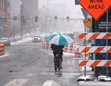 A bicyclist makes his way west on Market Street, protected from the heavy wet snow by an oversized umbrella. (Emma Lee/WHYY)