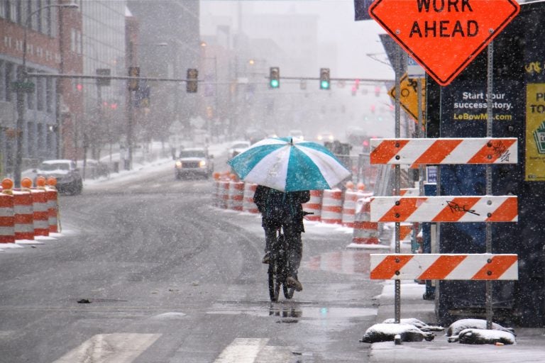 A bicyclist makes his way west on Market Street, protected from the heavy wet snow of the latest nor'easter by an oversized umbrella. (Emma Lee/WHYY)
