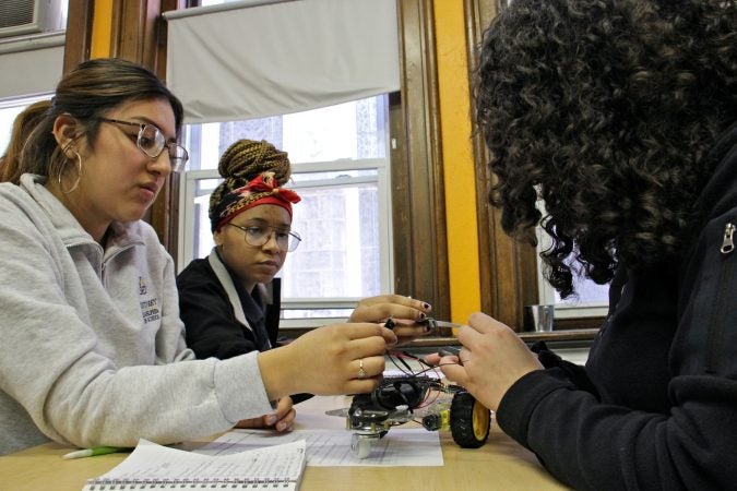 Cristo Rey students (from left) Kimberly Rangel, Briana Wells, and Marilyn Mejia check the wiring on their vehicle. (Emma Lee/WHYY)