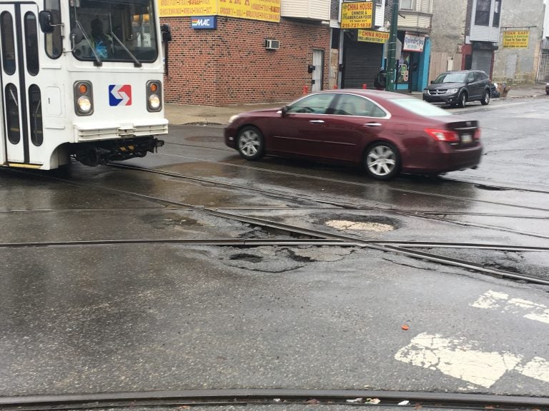 A trolley in West Philadelphia crosses potholes on a bumpy street. (Malcolm Burnley for WHYY)