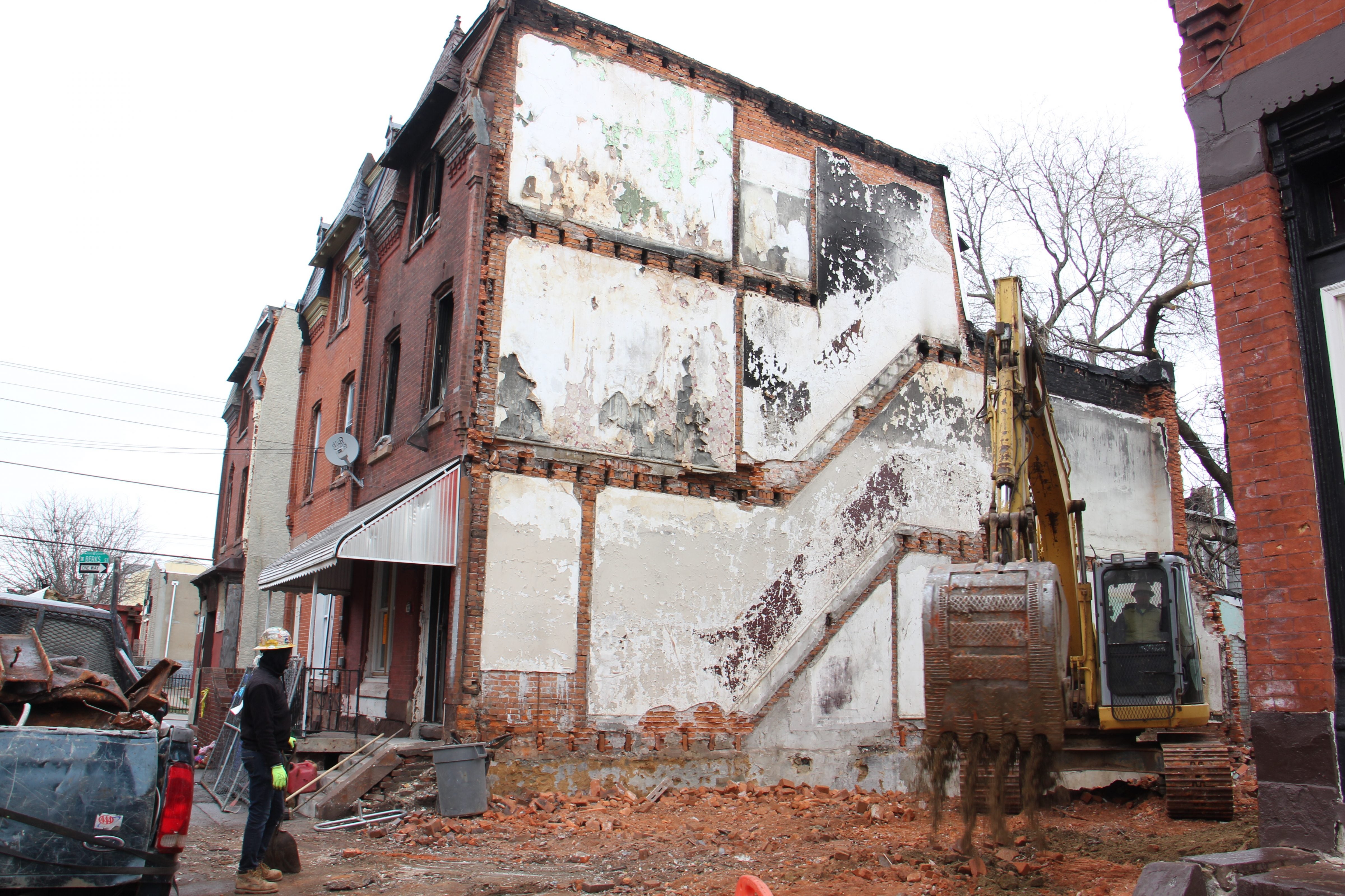 A backhoe works on the lot adjacent to 1855 N. 21st St., an illegal boarding house where 10 people are believed to have lived before a deadly fire struck last week.