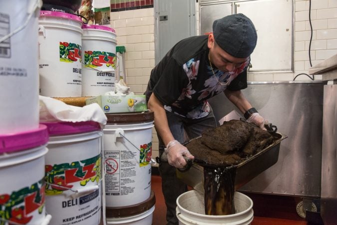 G pours out some of the juices from the Pastrami which has been in the oven since 3pm the day before. (Emily Cohen for WHYY)