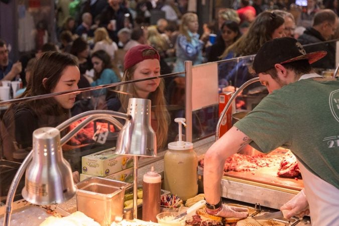 Ian McClendon, 23, finishes up a sandwich as two patrons look on longingly at their lunch. (Emily Cohen for WHYY)