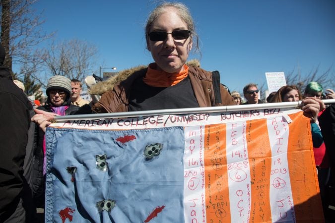 Debbie Collins, of Upper Providence, holds up her 3x5 flag which is completely covered with the dates of school shootings from all over the country and their number of victims in circles; the flag is full. (Emily Cohen for WHYY)