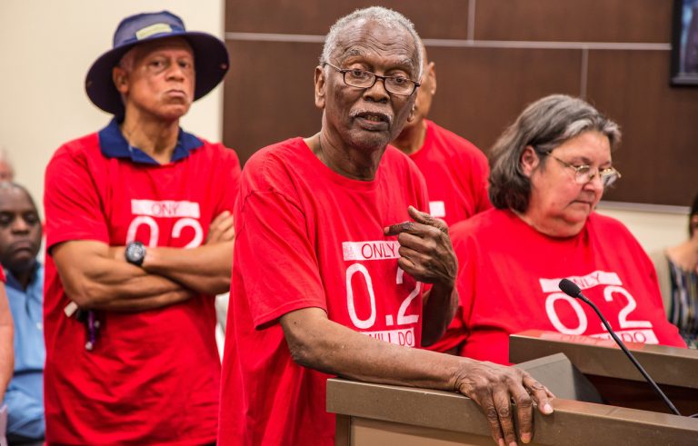 Robert Taylor, (center), speaks at a St. John the Baptist Parish council meeting in 2017. He and the other members of the citizens' group around him wear T-shirts that reference the safety limit for the chemical chloroprene. (Julie Dermansky)