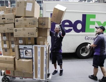 FedEx workers sort boxes for delivery on a busy street.