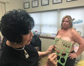 Rose Marie Beauchemin Verzella uses a template to pick the size of Maureen Matteis-Bilbee’s nipple and areola tattoos. (Alex Stern for WHYY) 