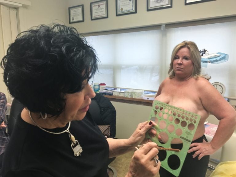 Rose Marie Beauchemin Verzella uses a template to pick the size of Maureen Matteis-Bilbee’s nipple and areola tattoos. (Alex Stern for WHYY) 