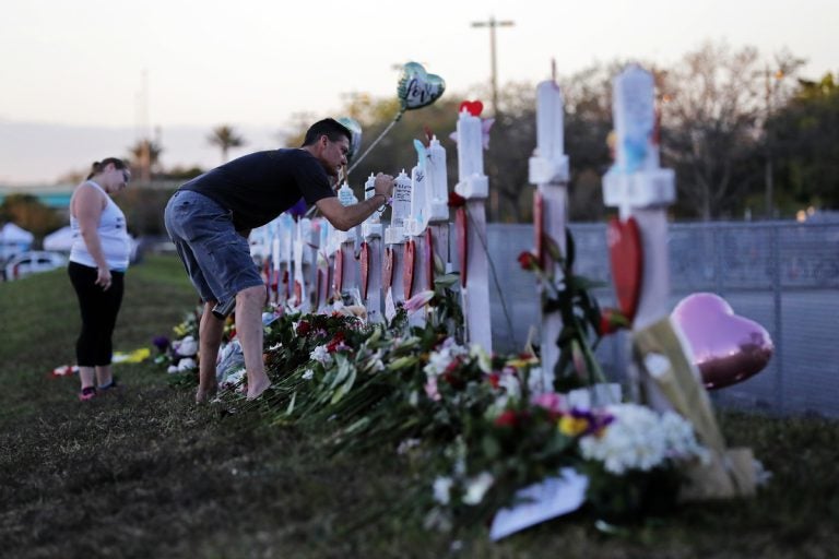 Paul Birmingham, on Monday, Feb. 19, 2018, writes on a cross placed in memory of student Gina Montaldo outside of Marjory Stoneman Douglas High School