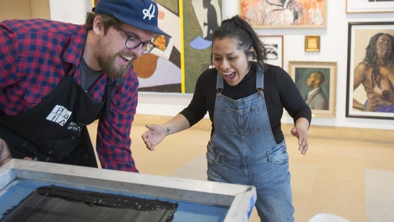 Ben Grzenia assists Jessica Aquino in creating a silk screen protest print. (Jonathan Wilson for WHYY)