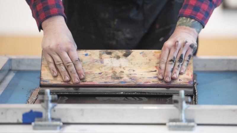 Ben Grzenia demonstrates how to squeegee a silk screen print. (Jonathan Wilson for WHYY)