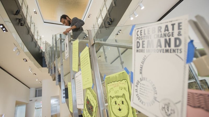 Stephen Coleman hangs posters on the main staircase of the Hamilton Building. (Jonathan Wilson for WHYY)