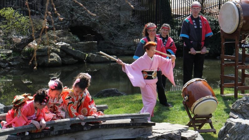 Fumiyo Batta, an instructor at the Japanese Language School of Philadelphia, beats a taiko drum while her students watch the koi fish in the pond at the Japanese House and Garden. (Emma Lee/WHYY)