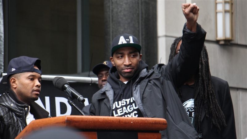 Hip-hop artist Mysonne Linen (center), who spent seven years in prison, supports Meek Mill during a rally, sharing the stage with activist lawyer Angelo Pinto (left). (Emma Lee/WHYY)