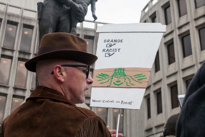 Demonstrator Mike Heisey holds a sign in front of the Philadelphia Police Department Headquarters on Race Street before a march in response to an incident where two black men were arrested in a Starbucks in Center City Philadelphia. (Brad Larrison for WHYY)