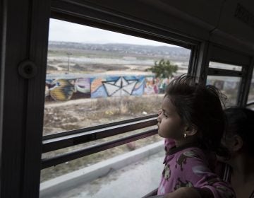 A Central American child who is traveling with a caravan of migrants, peers at the border wall from a bus carrying the group to a gathering of migrants living on both sides of the border, in Tijuana, Mexico, on April 29. (AP Photo/Hans-Maximo Musielik)