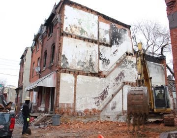 A backhoe operates on the lot adjacent to 1855 N. 21st St. in Philadelphia where four people died in a fire last month. (Emma Lee/WHYY)