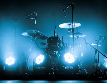 A kit of drums and a microphones on an empty stage in blue smoke before the concert