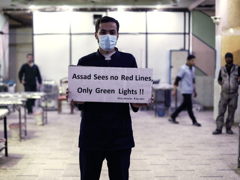 A medical worker at a Damascus hospital holds a sign protesting a suspected chemical weapons attack outside the Syrian capital a year ago. The suspected attacks led the U.S. to fire a barrage of missiles at a Syrian air base on April 7, 2017. (Sameer Al-Doumy/AFP/Getty Images)