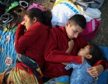 In this April 4, 2018 photo, the Zelaya siblings, from El Salvador, Nayeli, right, Anderson, center, and Daniela, huddle together on a soccer field, at the sports club where Central American migrants traveling with the annual 