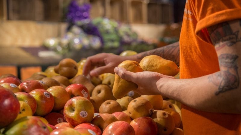 Alex Veal, 28, stacks some pears at Iovine Brothers produce store in Reading Terminal Market. (Emily Cohen for WHYY)