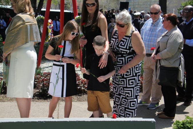 Family members place red carnations at the memorial, beside their loved ones names. (Emma Lee/WHYY)