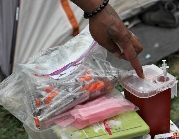 A resident of the Kensington Avenue encampment shows how he safely disposes of his used needles. (Emma Lee/WHYY)