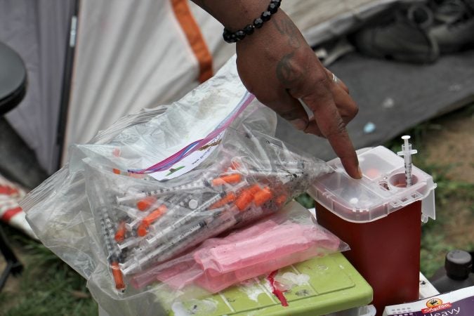 A resident of the Kensington Avenue encampment shows how he safely disposes of his used needles. (Emma Lee/WHYY)