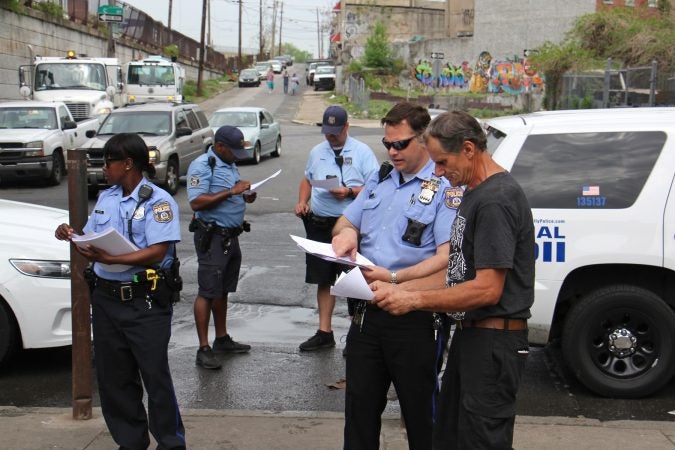 Police hand out flyers at Kensington Avenue and Tusculum Street, ordering residents of the heroin encampment there to leave by May 30. (Emma Lee/WHYY)