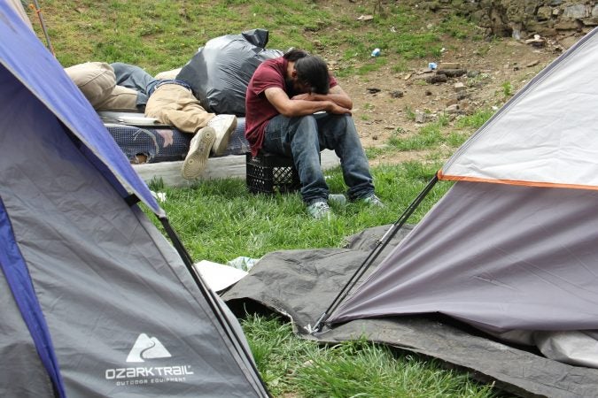 Residents of an encampment on Kensington Avenue wait with their possessions on a vacant lot while the city does a bi-weekly cleaning under the train overpass. (Emma Lee/WHYY)