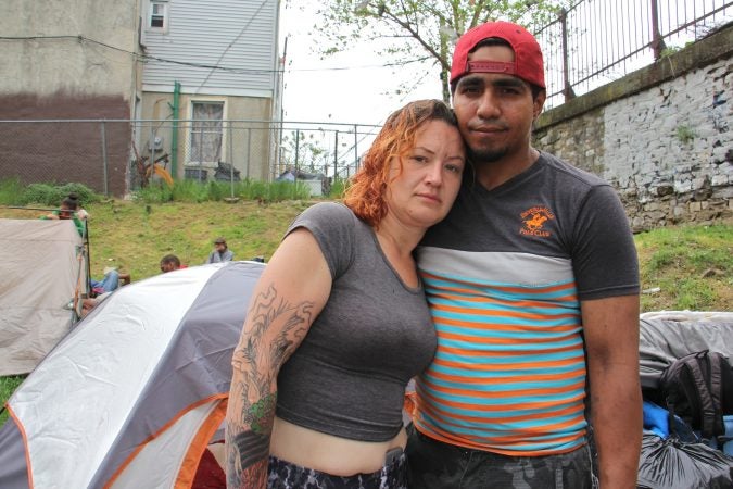 Salvatore Gonzalez and his fiancée stand in front of their tent near the Kensington Avenue railroad overpass, where heroin addicts have taken shelter since camp along the Conrail tracks near Gurney Street was shut down. (Emma Lee/WHYY)