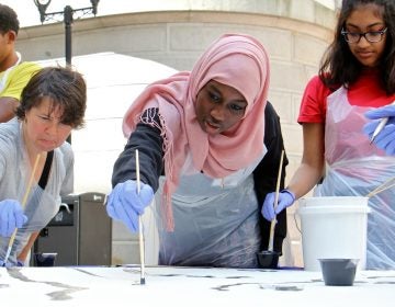 Masterman High School student Shahla Mukhtar (center) helps to paint a portion of the Octavius Catto mural. (Emma Lee/WHYY)