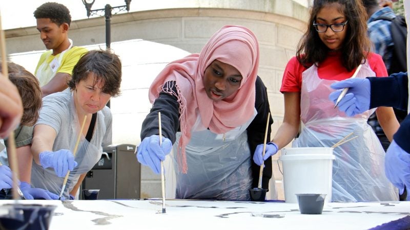 Masterman High School student Shahla Mukhtar (center) helps to paint a portion of the Octavius Catto mural. (Emma Lee/WHYY)