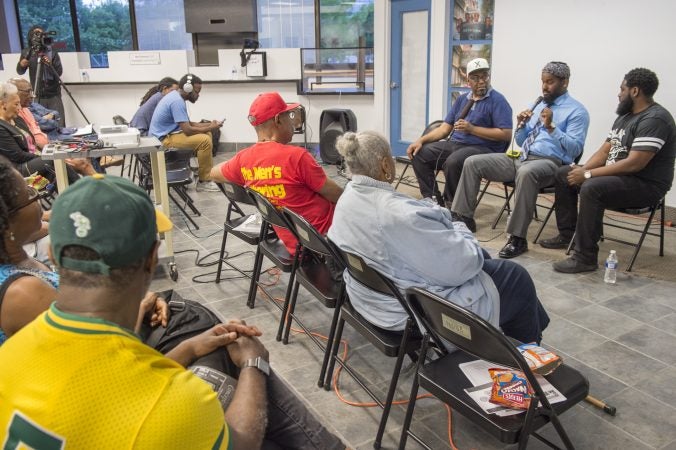 About two dozen people listen to community leaders discuss the legacy of Malcolm X. Speakers (from left) are moderator Michael Dennis, Mujahideen Mohammed, and B. F. Nkrumah. (Jonathan Wilson for WHYY)