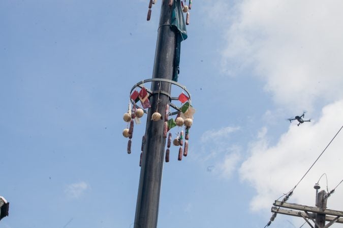 Prizes hang from the top of the grease pole at the Italian Market Festival as a drone hovers nearby Sunday. (Brad Larrison for WHYY)