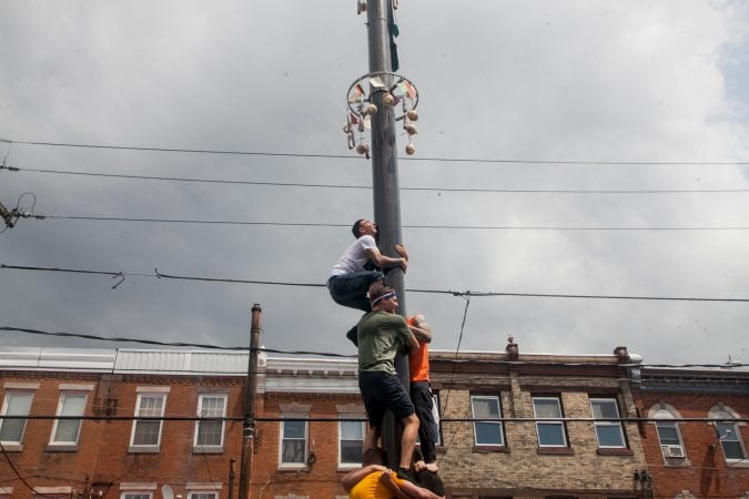 Nick Cordisio climbs on to his teammates shoulders as he tries to make it to the top of the grease pole. (Brad Larrison for WHYY)