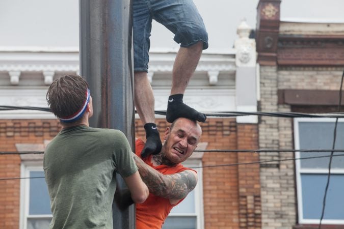 Escher, of the South Philly team, get his head stepped on by teammate Chris Cordisio Sunday as they ascended the grease pole. (Brad Larrison for WHYY)