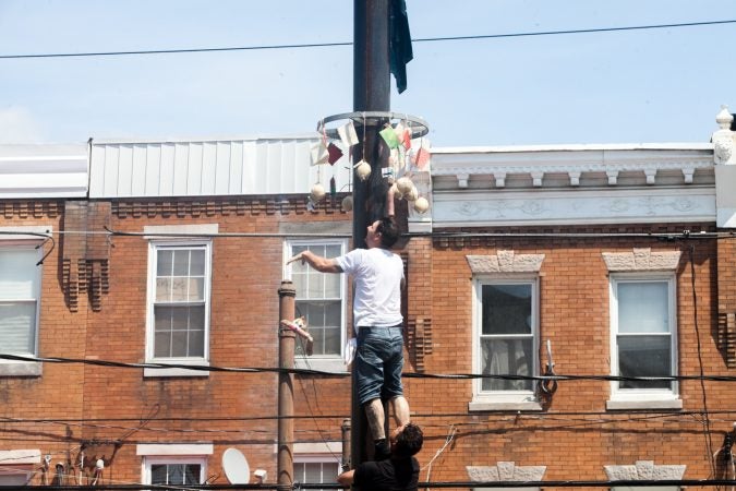 Nick Cordisio climbs on to his teammates shoulders and tosses a piece of cured meat that hung from the top of the grease pole. (Brad Larrison for WHYY)