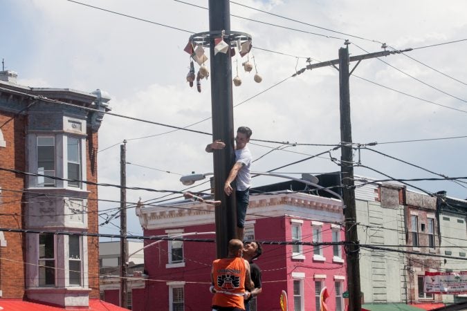Nick Cordisio climbs on to his teammates shoulders and tosses a piece of cured meat that hung from the top of the grease pole. (Brad Larrison for WHYY)
