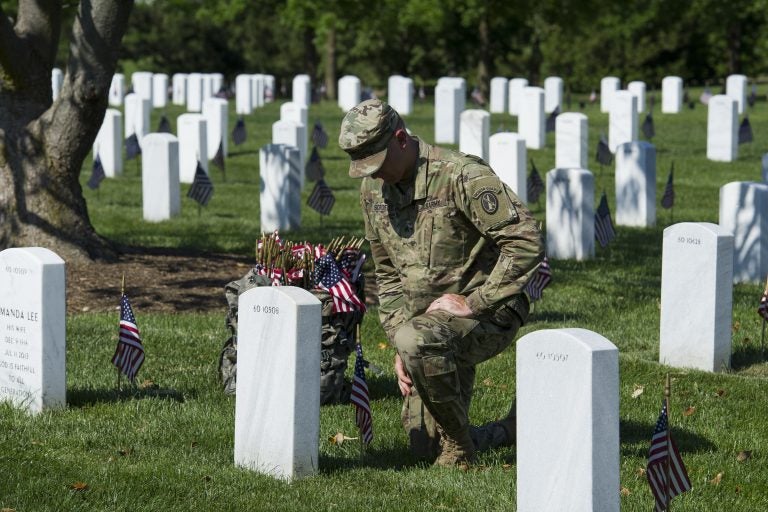 A member of the Army 3d U.S. Infantry Regiment, The Old Guard, pauses to honor a fallen soldier while places flags a the gravesite of the nation's fallen military heroes during its annual Flags In ceremony at Arlington National Cemetery, Thursday, May 24, 2018, in Arlington, Va. (AP Photo/Cliff Owen)