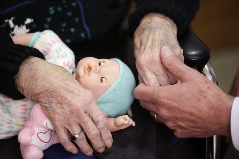 In this April 14, 2016, file photo, a son, (at right), holds his mother's hand at her nursing home in Michigan. Most young adults haven’t given much thought to their own needs as they get older, but a significant number are already providing long-term care for older loved ones, according to a new poll by the Associated Press-NORC Center for Public Affairs Research.   (Carlos Osorio/AP Photo, File)