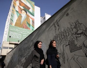 Iranian women walk past a portrait of the late revolutionary founder Ayatollah Khomeini and paintings of Persian poetry in Tehran, Iran, Monday, May 7, 2018. (Vahid Salemi/AP Photo)