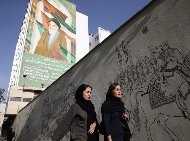 Iranian women walk past a portrait of the late revolutionary founder Ayatollah Khomeini and paintings of Persian poetry in Tehran, Iran, Monday, May 7, 2018. (Vahid Salemi/AP Photo)
