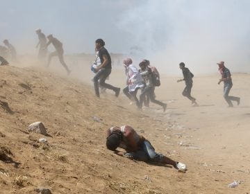 Palestinian demonstrators run or take cover from tear gas fired by Israeli forces at the Israel-Gaza border. (Ibraheem Abu Mustafa/Reuters)