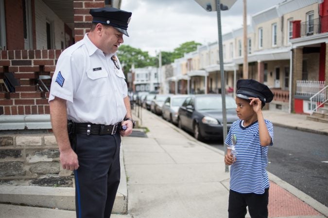 Sergeant Frank Kelly, of the 19th district, plays with Swyhir Crew, 7, who was inside his home down the street from where his teenage cousin and another boy were shot and his neighbor, 17-year-old Sandrea Williams, was killed on May 11, 2018. (Emily Cohen for WHYY)