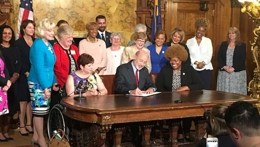 Gov. Tom Wolf signs an executive order, surrounded by supporters of the measure. (Katie Meyer/WITF)