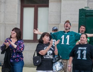 Mary Velez, center, her daughter Elen, right, and other Eagles fans sing the team's fight song at a rally for the team at City Hall Tuesday evening a day after President Trump canceled an event at the White House to honor the Super Bowl Champions. (Brad Larrison for WHYY)