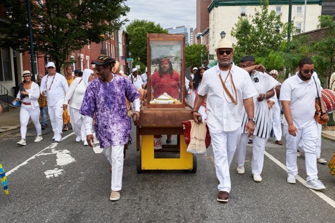 Akmal Muwwakkil (left) and Kerwin Capers (right) lead the empty procession stand back to the Odunde Festival in Philadelphia after offerings were given to the Schuylkill River on Sunday, June 10, 2018. The offerings included flowers, fruit, cake, and incense, amongst other biodegradable goods. (Natalie Piserchio for WHYY News) 