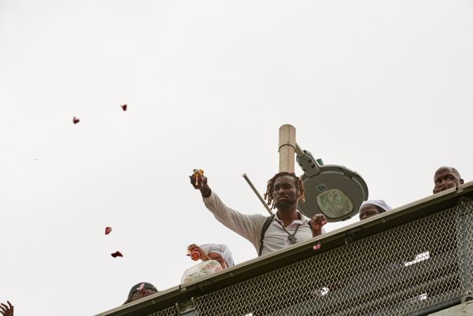 Participants of the processesion at 2018 Odunde Festival in Philadelphia cast offerings into the Schuylkill River off of the South Street Bridge. Offerings include honey, fruit, flowers, cake, and other biodegradable goods. (Natalie Piserchio for WHYY News) 